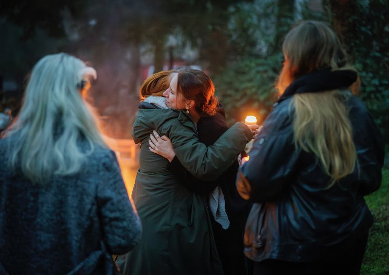 Zwei Frauen umarmen sich am Feuer, eine hält eine Kerze